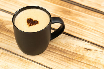 Top view of hot latte or cappuccino coffee in black cup with heart inside on wooden table background