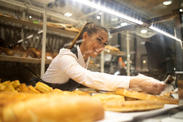 Woman preparing pastry for sale in supermarket bakery department.