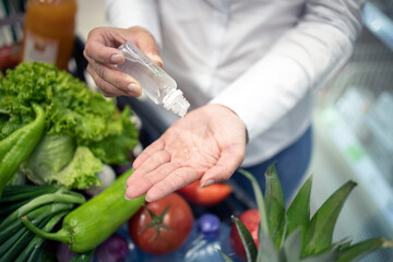 Hands sanitizing against corona virus while shopping in supermarket. Close up view of hands rubbing disinfection to stay healthy. Covid-19 protection measures.