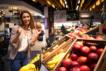 Positive brunette woman holding coconut at grocery store fruit department. Buying fruit at supermarket.