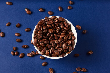 Coffee Beans in white cup spilling over to the blue background 