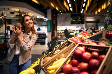 Positive brunette woman holding coconut at grocery store fruit department. Buying fruit at supermarket.
