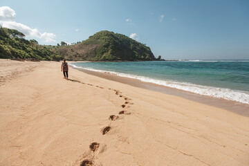 Back view of a woman with a backpack on the ocean on nature, walk on empty sand beach, leaving footprints