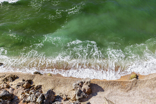 Top View Of The Sea Coast With Green Water And Surf On A Sandy Beach.