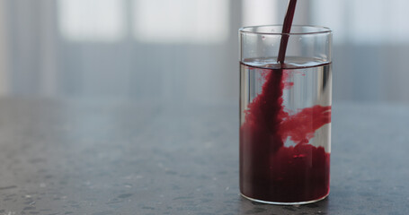Pour berry juice into glass with water on concrete countertop