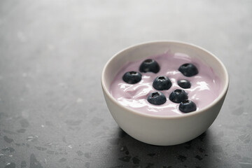 Blueberry yogurt with whole berries in white bowl on concrete background