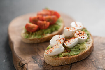 Bruschettas with avocado, tomato and mozzarella on wood board on concrete bacground