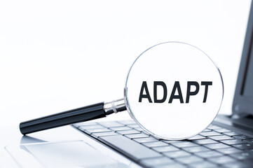 Magnifier with text ADAPT on the background of a laptop keyboard.