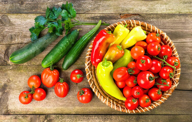 Harvest of fresh ripe vegetables on wooden table and in rod bowl - pepper, tomato, cucumber, celery leaves. Healthy organic food, summer vitamins, BIO viands, natural background. Top view