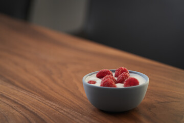 Yogurt with fresh raspberries in blue ceramic bowl on walnut table with copy space