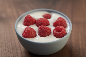 Yogurt with fresh raspberries in blue ceramic bowl on walnut table