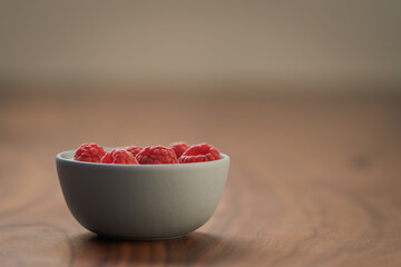 Yogurt with fresh raspberries in blue ceramic bowl on walnut table