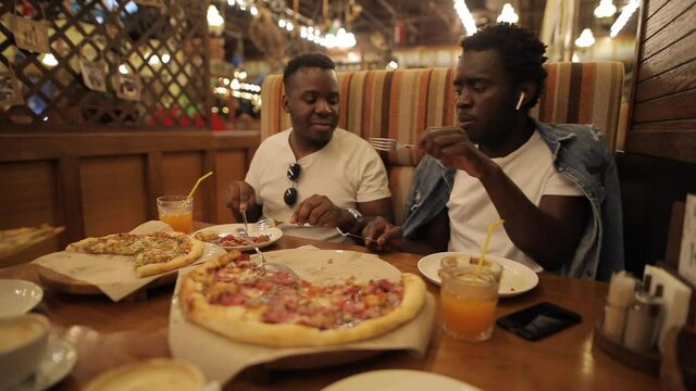 Two African American guys in white T-shirts eat funny pizza in a restaurant