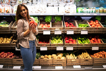 Woman standing by the shelf full of vegetables and holding tomatoes. Healthy food promotion.