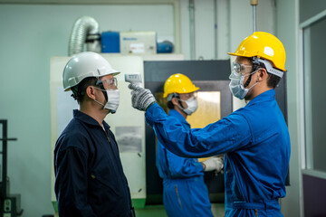 Industrial worker wear protective face mask scan temperature before working at factory to protect infection from coronavirus covid-19, social distancing concept.