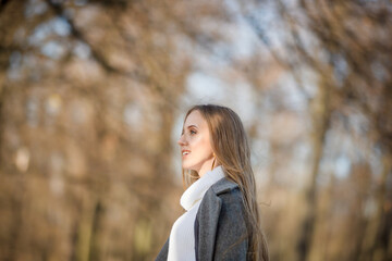Pretty woman with light brown hair. Portrait of a beautiful smiling woman in an elegant gray coat. Happy young woman walks in the autumn park.