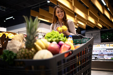 Woman filling up shopping cart with fruit and healthy food. Weekend grocery shopping at supermarket.