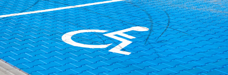 Empty blue parking spot for the handicapped, wheelchair symbol on the ground, wide panoramic shot. Parking place for the disabled. Parking lot area outdoors, closeup. Simple accessibility concept