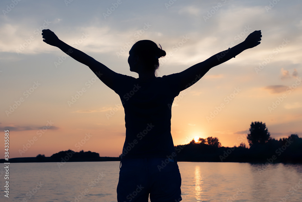 Wall mural silhouette of carefree woman with arms outstretched on the beach at sunset.