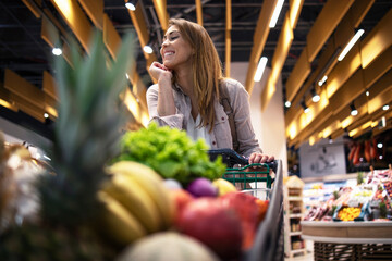 Grocery shopping. Female person standing by the shopping cart and smiling. Buying healthy food at...