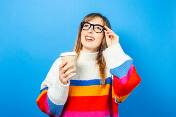  young girl holds a cardboard cup with coffee and shows emotions, joy, happiness on a blue background. Banner