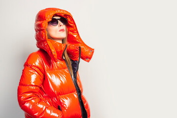 happy young girl in a red jacket and sunglasses, looks up on a light background. Concept of casual fashion, shopping, trend