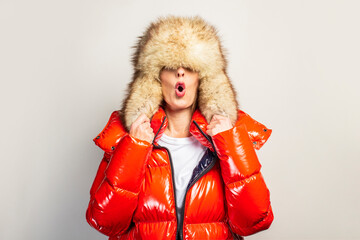 surprised beautiful young girl in a red jacket and fur hat, hat closes her eyes on a light...