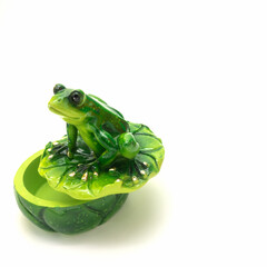 Ceramic casket for storing small items. A lid in the form of a water lily leaf on which a green frog sits. Big shiny eyes, gilded toes. Isolated on white background.
