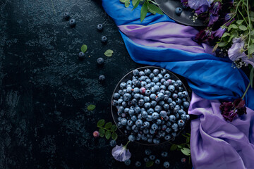 Summer still life with blueberries, colored sweet peas and meadow grasses on a dark blue table.
