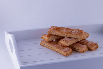 Stack of six delicious golden Puff Pastry fingers sprinkled with sugar on white tray with copy space