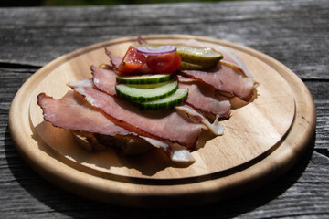 Delicious fresh bread with smoked bacon, cucumber, tomatoes and red onions on wooden plate