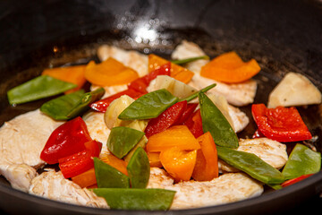 Slices of chicken breast are fried with vegetables: peppers, tomatoes, pea pods.