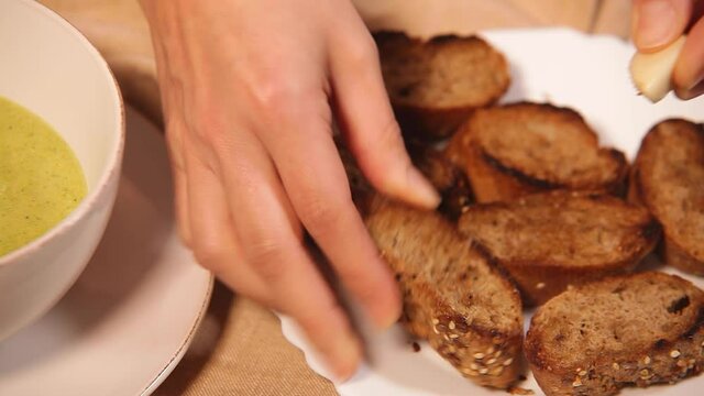Cook rubbing clove of garlic on fried dried up pieces of bread making canapes. Food concept.