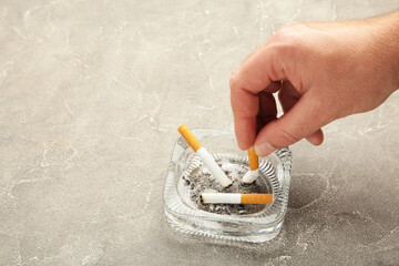 A hand puts out a cigarette in an ashtray on grey background.