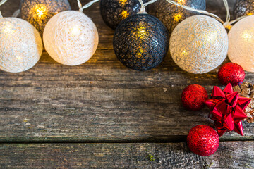 Christmas tree decoration balls with warm yellow light on aged weathered pine wood boards, focus on the red decoration, space for text.