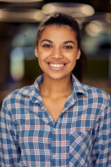 Vertical shot of a young happy mixed race business woman in casual wear looking at camera and smiling while posing in the office