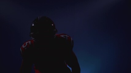 Portrait of determined professional American football player in helmet in bright stadium illumination lights ready for game. Confident man in red and white uniform. Usa extreme sport spirit concept.