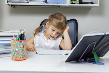 tired little girl sitting at a desk and holding hands to head. baby 4-5 years. on the desk a lot of...