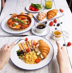 Breakfast is served on a light board. Fried eggs, omelet, croissant, coffee, dessert, place for text.