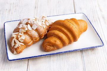 Two croissants in a plate on a light board