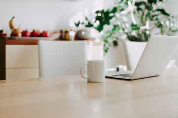 Open laptop and cup of coffee on table in living room, strong window light. Working at home concept.