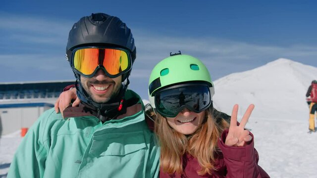 Two best friends, man and woman on top of mountain, near ski lift on sunny day look into camera, pose for photos. Authentic real people have fun, laugh and smile during snowboard or ski vacation