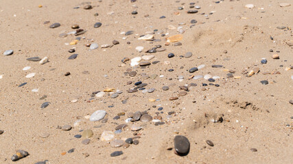 Big flat stones scattered on a yellow sandy beach. Texture sand mound of sand. Colored small rocks on beach sand