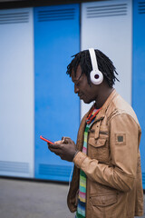 Young Black Man using smartphone and headphones to chat and to listen to music. Guy wearing casual...