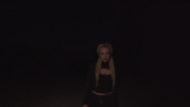 Creepy bloodthirsty woman vampire with dreadlocks walking on dirt road in darkness, frightening and hissing, showing her bloody pale face, expressing aggression and fear during haunting on halloween.