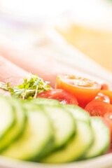 Sandwich fillings for lunch - sliced cucumber, tomatoe and ham on white plate