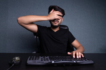 the young man covered his face with his hand. Sits in front of the monitor.