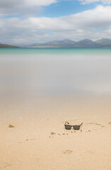 Empty sand beach in front of summer sea with sunglasses, holiday background with copy space