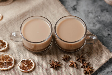 Two identical cups of hot cocoa are on the table. Under them is a napkin made of natural material, next to it lies star anise and slices of dried lemon.