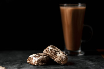 Two gingerbread cookies are on the table. In the background, a large glass with a brown drink. Without man. Artistic effect of a blurred background.